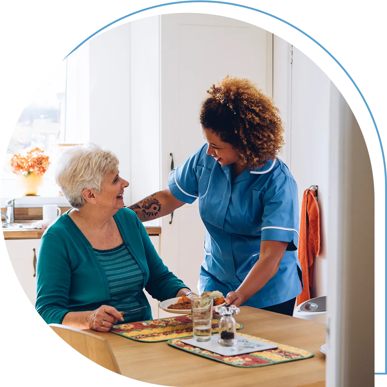 Caregiver assisting elderly woman at kitchen table.